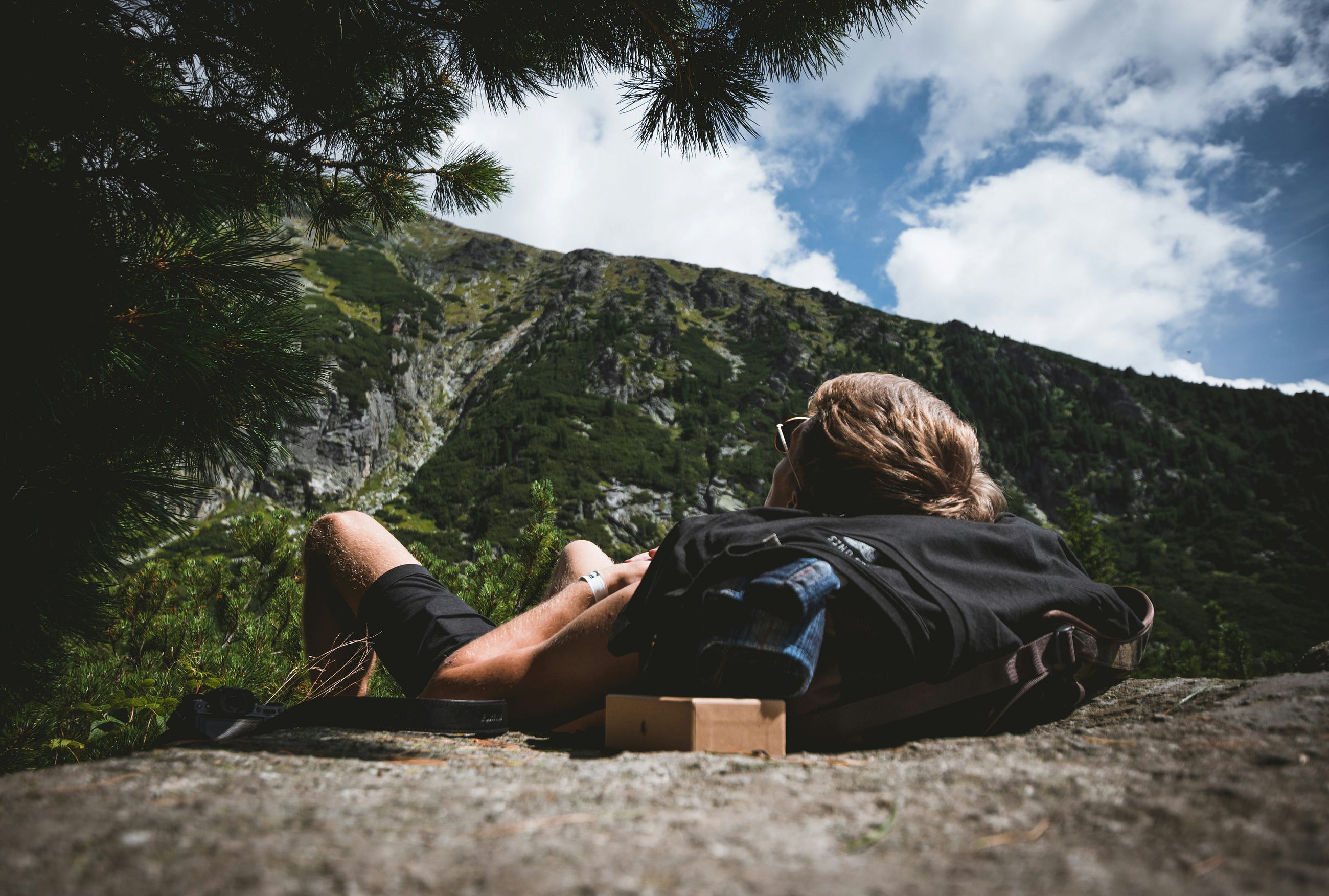 A person lying on the ground facing a mountainous landscape, symbolizing stress and exhaustion in nature.