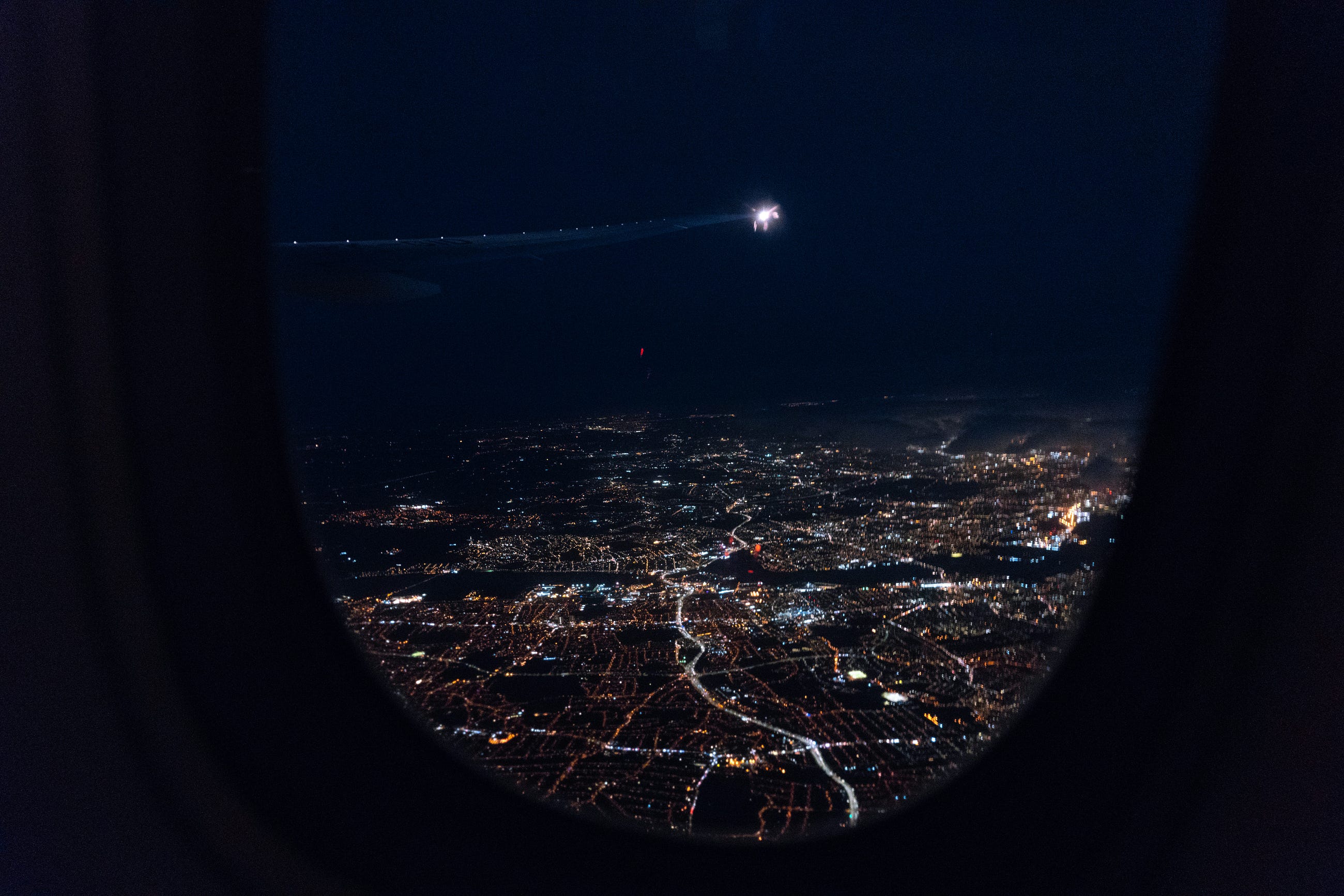 Gece yarısı uçak penceresinden şehrin aydınlık binalarının ve yollarının kuşbakışı görünümü.
