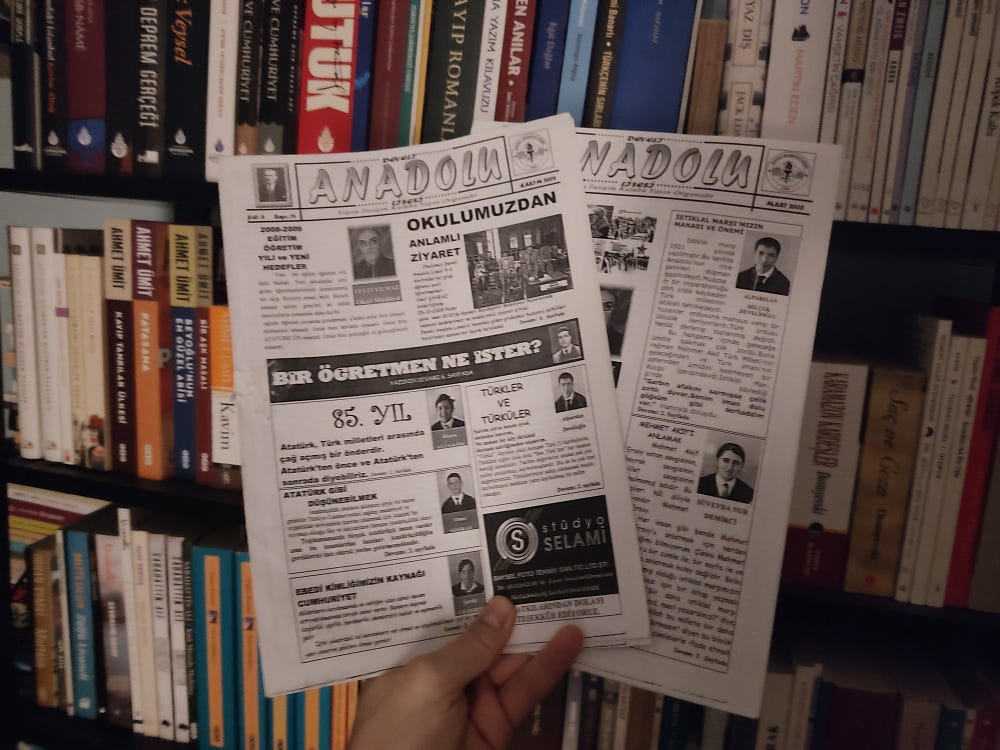 Two pages of Turkish 'Anadolu' newspaper held in someone's hands with bookshelves visible in the background.