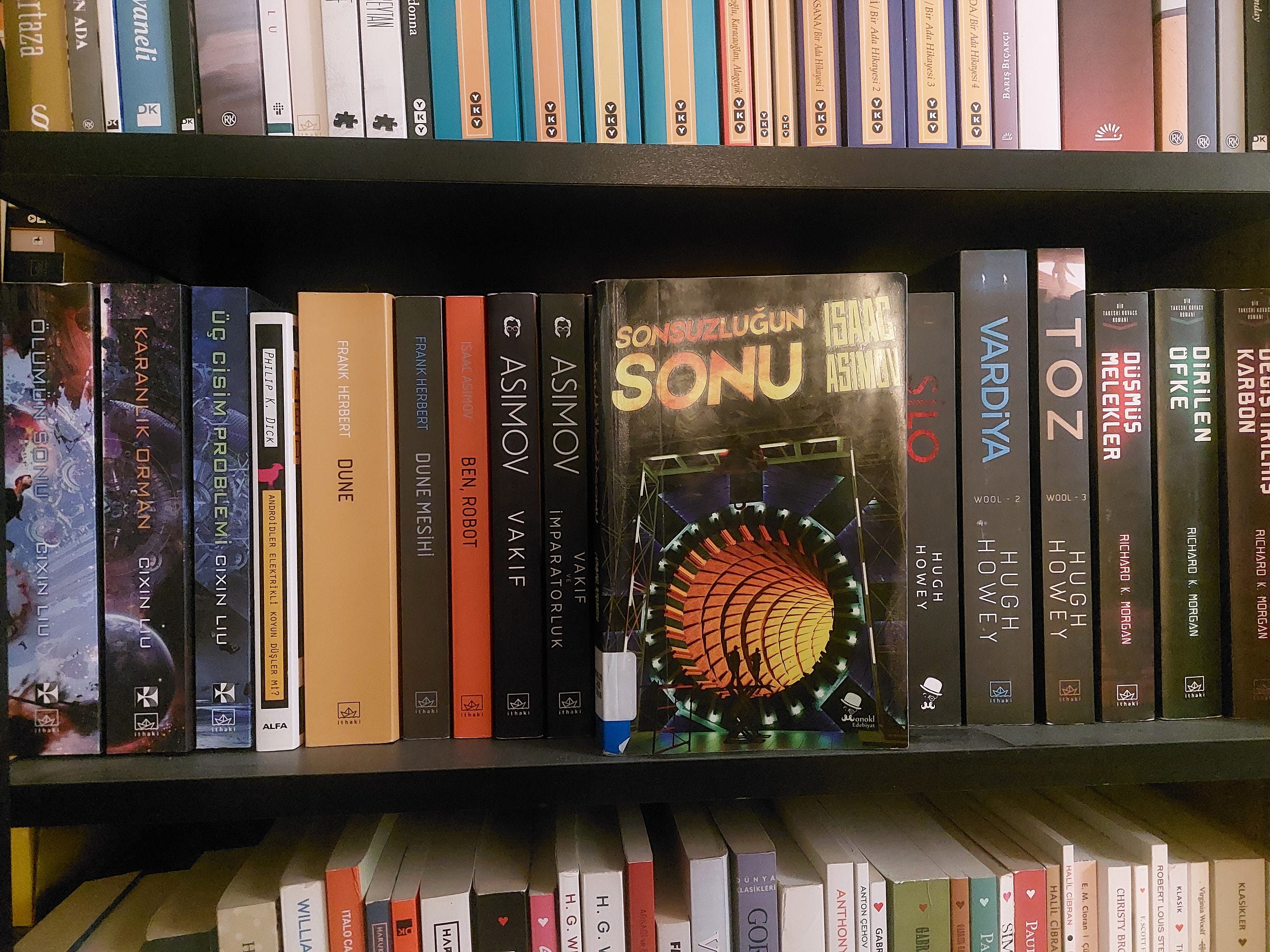 Bir kütüphane rafında bilim kurgu kitapları, ortada 'Son Zaman Sonu' başlıklı kitap öne çıkıyor.