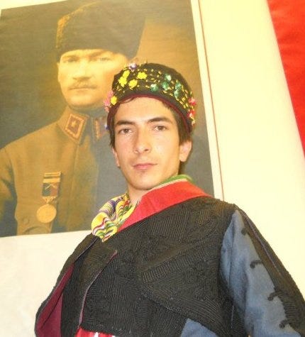 A young man wearing traditional clothing poses while wearing a colorful headband.